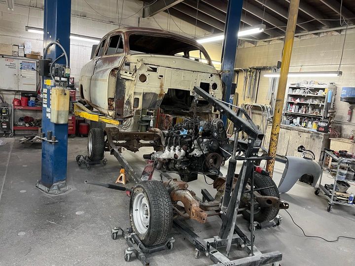Vintage sedan body raised on a lift in the shop, its frame and running gear on dollies below