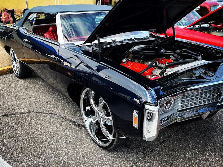 Black Chevy Impala convertible with the hood up and a red engine bay, at a street car show